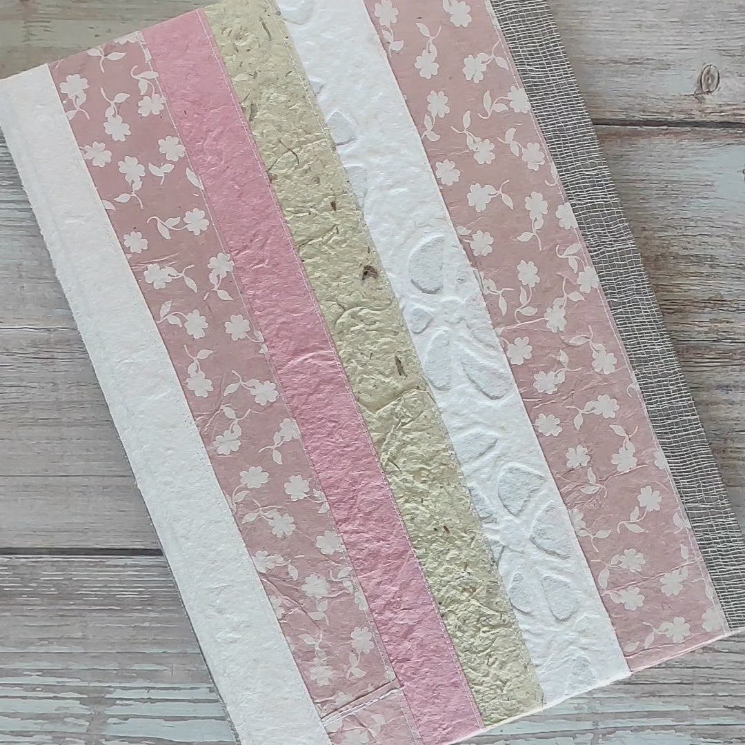 Diario rilegato con copertina rigida rivestita con un patchwork di carte artigianali cucite tra loro. Tonalità rosa, bianco e naturale.